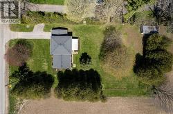 Property featuring a detached residence with a dark-toned shingle roof, expansive green lawn, and a gravel driveway - 