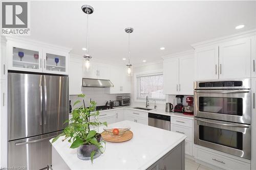 Two tone kitchen featuring stainless steel appliances, a center island, pendant lighting, light stone countertops, and crown molding - 89 Lynnhaven Court, Kitchener, ON - Indoor Photo Showing Kitchen With Upgraded Kitchen