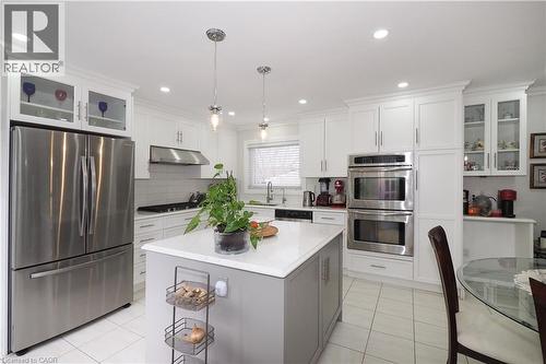 Dual tone kitchen with glass fronted cabinets, stainless steel appliances, a center island, decorative light fixtures, and backsplash - 89 Lynnhaven Court, Kitchener, ON - Indoor Photo Showing Kitchen With Upgraded Kitchen