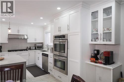 Kitchen with tasteful backsplash, decorative light fixtures, white cabinetry, stainless steel appliances, and glass fronted cabinets - 89 Lynnhaven Court, Kitchener, ON - Indoor Photo Showing Kitchen