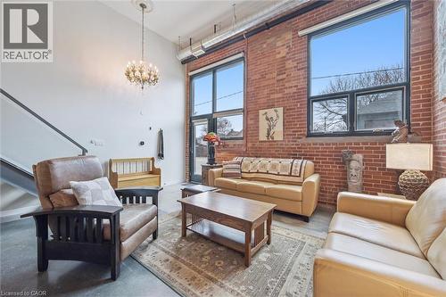 Living area featuring a high ceiling, concrete flooring, brick wall, and a chandelier - 85 Spruce Street Unit# 106, Cambridge, ON - Indoor Photo Showing Living Room