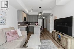 Open-concept living space featuring wood-finish flooring, a kitchen with grey shaker cabinetry, stainless steel appliances, and a tiled backsplash - 