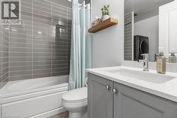 Modern main bathroom featuring grey subway tile tub surround, white bathtub, and a single vanity with a white composite countertop and grey cabinetry - 