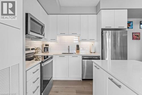 Kitchen featuring appliances with stainless steel finishes, backsplash, white cabinetry, light wood-style floors, and light stone counters - 385 Winston Road Unit# 1402, Grimsby, ON - Indoor Photo Showing Kitchen With Upgraded Kitchen