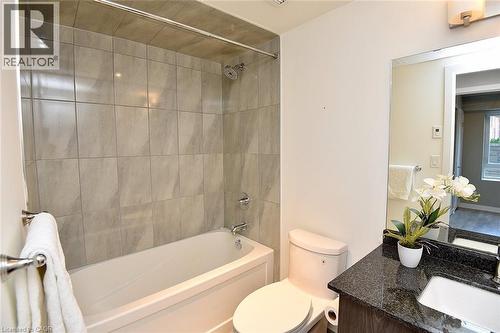 Bathroom featuring a tub/shower combination with light-toned wall tiles, a dark granite-style countertop, and a wood-finish vanity with an undermount sink - 16 Markle Crescent Unit# 111, Ancaster, ON - Indoor Photo Showing Bathroom