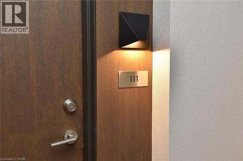 Solid wood-grain door with brushed nickel hardware, illuminated by a modern black wall-mounted fixture - 16 Markle Crescent Unit# 111, Ancaster, ON - 