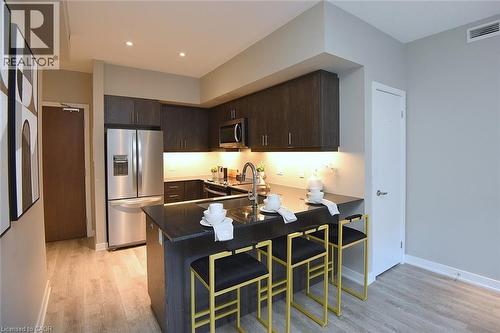 Modern kitchen featuring dark wood-finish cabinetry, stainless steel appliances, a black countertop island with breakfast bar seating, and recessed lighting - 16 Markle Crescent Unit# 111, Ancaster, ON - Indoor Photo Showing Kitchen With Double Sink