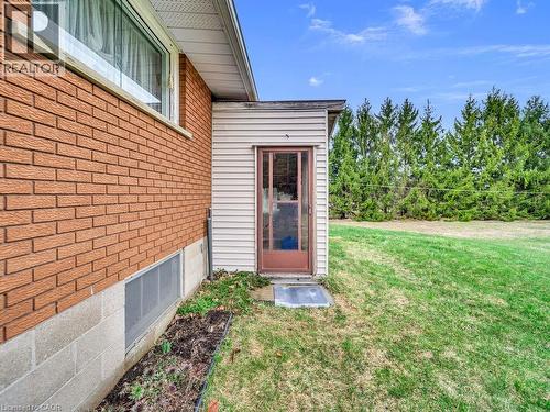 Brick exterior with a window well, a privacy screen of mature trees, and a side entry with a glass-paneled door - 1416 Highway 6, Hamilton, ON - Outdoor With Exterior