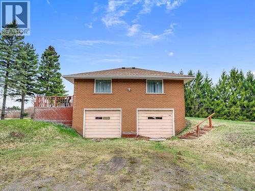 Brick exterior residence featuring two garage bays, a side deck with railing, and a sloped grassy area - 1416 Highway 6, Hamilton, ON - Outdoor With Exterior
