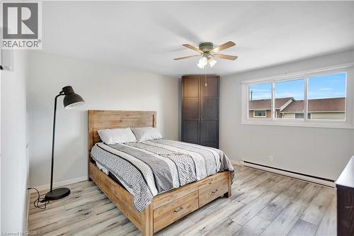 Light-filled interior featuring wood-finish flooring, a ceiling fan with integrated lighting, a corner built-in closet with dark wood-finish doors, and a multi-pane window - 32 Montclair Crescent, Simcoe, ON - Indoor Photo Showing Bedroom