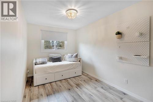 Bright room featuring a window with roller shade, wood-finish flooring, and a decorative ceiling light fixture - 32 Montclair Crescent, Simcoe, ON - Indoor Photo Showing Bedroom