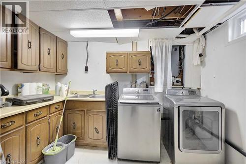 Laundry area featuring wood cabinetry, a dual-basin sink, and a high-level window - 32 Montclair Crescent, Simcoe, ON - Indoor Photo Showing Laundry Room