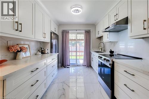 Contemporary kitchen featuring white shaker cabinetry, stone countertops, a full-height stone backsplash, stainless steel appliances, and large format tile flooring - 103 East 45Th Street, Hamilton, ON - Indoor Photo Showing Kitchen With Upgraded Kitchen