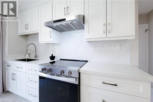 White shaker cabinetry with brushed nickel hardware, stainless steel range with overhead ventilation, undermount sink with gooseneck faucet, and stone countertops extending to a full-height backsplash - 103 East 45Th Street, Hamilton, ON - Indoor Photo Showing Kitchen With Upgraded Kitchen