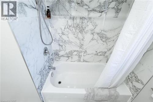 White soaking tub with chrome fixtures, surrounded by large format marble-look tile walls - 103 East 45Th Street, Hamilton, ON - Indoor Photo Showing Bathroom