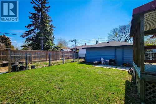 Expansive backyard featuring a lush lawn, privacy fencing, a separate storage structure with a shingled roof, a paved patio area, and a covered wood-decked patio - 103 East 45Th Street, Hamilton, ON - Outdoor