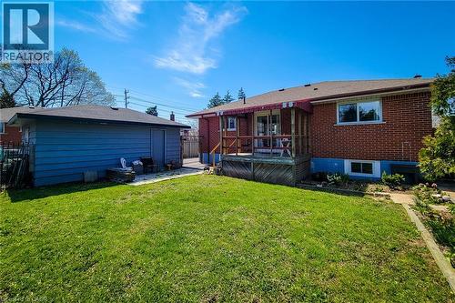 Spacious backyard featuring a detached garage with siding, a brick exterior home, a wooden deck with a red awning, and a grass lawn - 103 East 45Th Street, Hamilton, ON - Outdoor