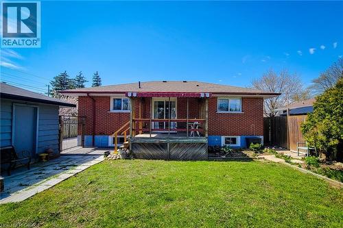 Expansive green lawn with a brick exterior home featuring a rear deck with a red and white striped awning - 103 East 45Th Street, Hamilton, ON - Outdoor