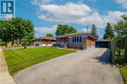 Bungalow-style residence featuring a brick and stone facade, an attached garage, a detached garage, a paved driveway, and a front lawn with mature trees - 103 East 45Th Street, Hamilton, ON - Outdoor