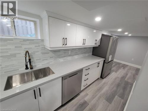 Modern kitchen featuring white cabinetry, light gray countertops, a stainless steel double sink with a flexible faucet, a matching dishwasher, and a refrigerator - 168 Garside Avenue N, Hamilton, ON - Indoor Photo Showing Kitchen With Double Sink