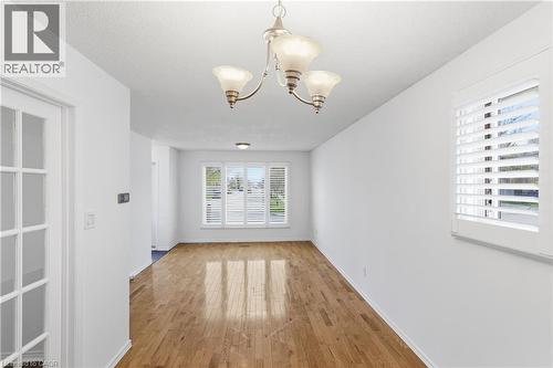 Spacious interior room featuring wood-finish flooring, white walls, and a multi-light chandelier - 341 Rexford Drive, Hamilton, ON - Indoor Photo Showing Other Room