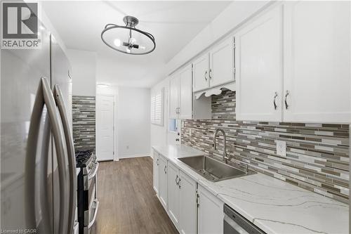 Galley kitchen featuring white cabinetry, a stainless steel sink with a gooseneck faucet, light-toned countertops, and a full-height mosaic tile backsplash - 341 Rexford Drive, Hamilton, ON - Indoor Photo Showing Kitchen With Stainless Steel Kitchen With Upgraded Kitchen