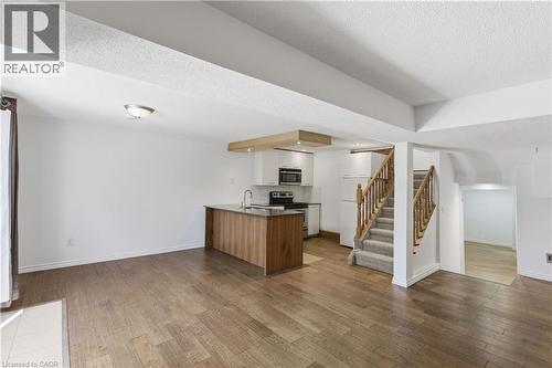 Open-concept living area with wood-finish flooring, a kitchen island, white cabinetry, stainless steel appliances, and a carpeted staircase with wood banisters - 341 Rexford Drive, Hamilton, ON - Indoor