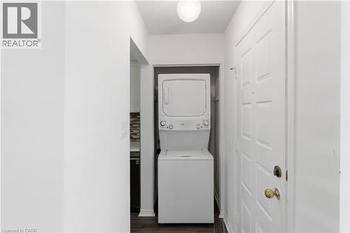 Entryway featuring wood-finish flooring, a white paneled door with brass hardware, and a stacked white washer and dryer unit - 341 Rexford Drive, Hamilton, ON - Indoor Photo Showing Laundry Room
