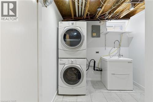 Dedicated laundry area featuring a stacked washer and dryer, utility sink with a gooseneck faucet, wall-mounted shelving, and a small window - 341 Rexford Drive, Hamilton, ON - Indoor Photo Showing Laundry Room