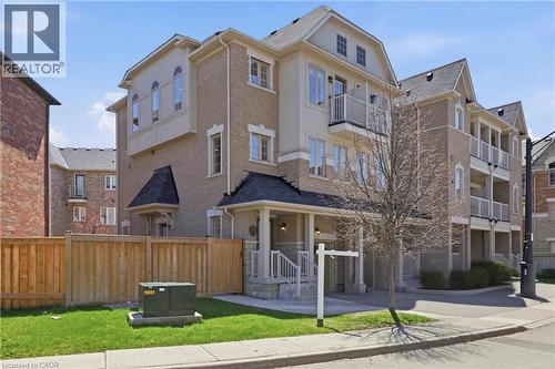 Multi-story townhouse featuring a brick and stucco exterior, multiple balconies with metal railings, a covered front porch with white columns, gabled rooflines, and a private fenced yard with green la - 9 Rabbit Run Way, Brampton, ON - Outdoor With Facade