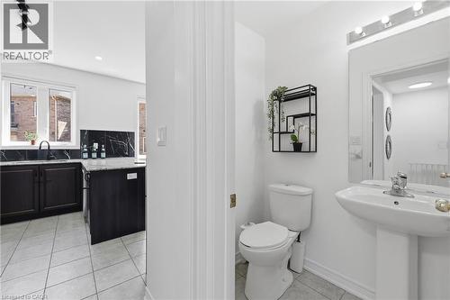 Modern half-bath with pedestal sink and overhead vanity lighting, featuring a contrasting kitchen beyond with dark cabinetry, patterned backsplash, and light-toned tile flooring - 9 Rabbit Run Way, Brampton, ON - Indoor Photo Showing Bathroom
