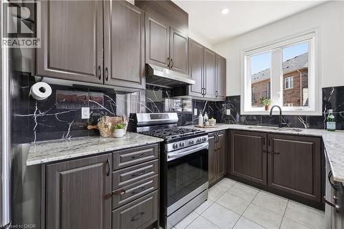 U-shaped kitchen featuring dark wood-finish cabinetry, light speckled countertops, and a black veined backsplash - 9 Rabbit Run Way, Brampton, ON - Indoor Photo Showing Kitchen