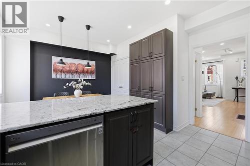 Kitchen featuring a granite countertop island with integrated dishwasher, dark wood-finish cabinetry, two pendant lights, and tile flooring - 9 Rabbit Run Way, Brampton, ON - Indoor Photo Showing Kitchen