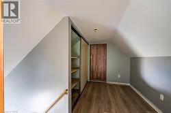 Loft space featuring wood-finish flooring, built-in shelving with sliding doors, a natural wood door, and sloped ceilings - 