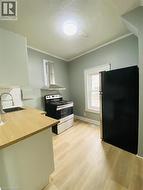 Unit 1A Kitchen featuring wood-finish flooring, light-toned cabinetry, stainless steel range with overhead ventilation, and a black refrigerator - 
