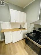 Unit 1A Kitchen featuring light wood-finish flooring, white shaker-style cabinetry, a stainless steel sink with a gooseneck faucet, light wood-finish countertops, and white subway tile backsplash - 
