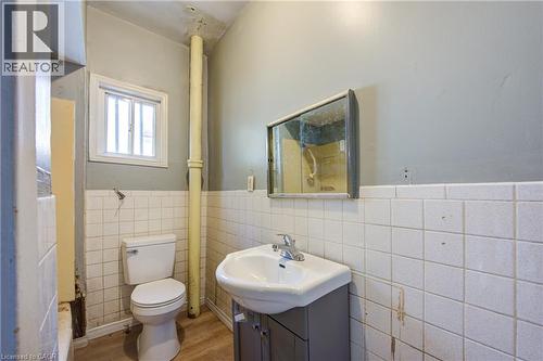 Unit 1B - 4 Pc Bathroom featuring a corner vanity with an integrated sink, a wall-mounted medicine cabinet, white square wall tiling, and wood-finish flooring - 1 Rathgar Street, London, ON - Indoor Photo Showing Bathroom