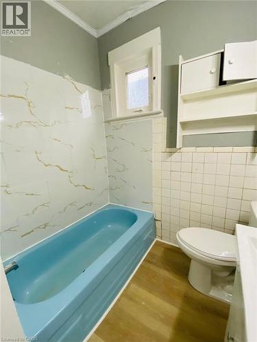 Unit 1A - 4 Pc Bathroom featuring a blue tub, white and gold-veined wall tiles, a window with frosted glass, and wood-finish flooring - 1 Rathgar Street, London, ON - Indoor Photo Showing Bathroom