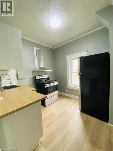 Unit 1A Kitchen featuring wood-finish flooring, light-toned cabinetry, stainless steel range with overhead ventilation, and a black refrigerator - 1 Rathgar Street, London, ON - Indoor Photo Showing Other Room
