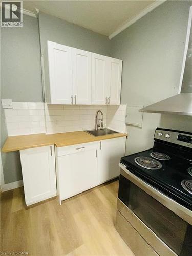 Unit 1A Kitchen featuring light wood-finish flooring, white shaker-style cabinetry, a stainless steel sink with a gooseneck faucet, light wood-finish countertops, and white subway tile backsplash - 1 Rathgar Street, London, ON - Indoor Photo Showing Kitchen