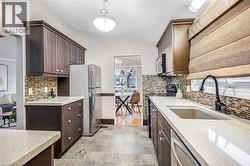 Kitchen featuring dark wood-finish cabinetry, light-toned countertops, a mosaic tile backsplash, and stainless steel appliances - 