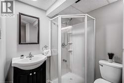 Compact bathroom featuring a corner shower with glass enclosure, pedestal sink with dark wood-finish vanity, wall-mounted mirror, and white toilet - 