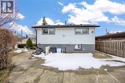 Rear exterior of the property featuring light-colored siding, a dark roof, and a partial concrete driveway - 