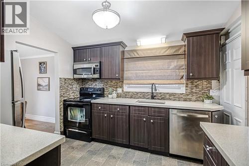 Contemporary kitchen featuring dark wood-finish cabinetry, light-toned countertops, a mosaic tile backsplash, stainless steel appliances, and diagonal tile flooring - 85 Ranchdale Drive, Hamilton, ON 