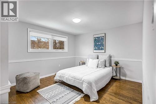 Bedroom featuring wood-finish flooring, two large windows, a white ceiling light fixture, and two-tone wall paint with chair rail trim - 85 Ranchdale Drive, Hamilton, ON 