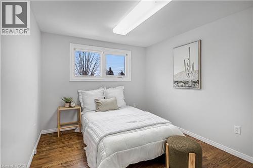 Bedroom featuring a window with natural light, wood-finish flooring, white baseboards, light grey wall paint, and a ceiling-mounted fluorescent light fixture - 85 Ranchdale Drive, Hamilton, ON 