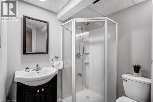 Compact bathroom featuring a corner shower with glass enclosure, pedestal sink with dark wood-finish vanity, wall-mounted mirror, and white toilet - 85 Ranchdale Drive, Hamilton, ON 
