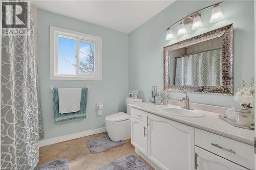Bathroom featuring a single vanity with white cabinetry and a light-toned countertop, a rectangular mirror with a decorative frame, and a four-light fixture - 79 Holbrook Crescent, Cambridge, ON - Indoor Photo Showing Bathroom