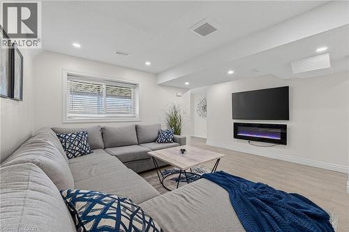 Bright living space featuring recessed lighting, a modern wall-mounted electric fireplace, wood-finish flooring, and a large window with blinds - 79 Holbrook Crescent, Cambridge, ON - Indoor Photo Showing Living Room