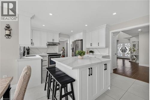 Bright kitchen featuring a central island with countertop seating, white shaker cabinetry, stainless steel appliances, and a matching stone backsplash - 79 Holbrook Crescent, Cambridge, ON - Indoor